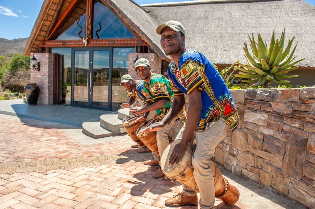 Traditional African drummers warmly welcoming guests at Mont Eco Private Nature Reserve, performing outside the lodge entrance in colourful attire.